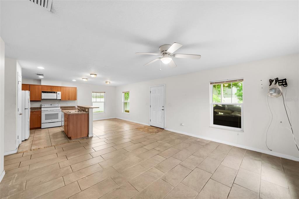 An open-concept living area features tile flooring, a ceiling fan, and an adjacent kitchen — 5451 MAC ARTHUR AVENUE, NEW PORT RICHEY, FL