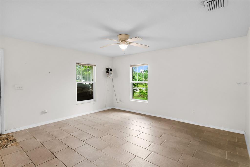 An empty room with light-colored walls, tile flooring, two windows, and a ceiling fan — 5451 MAC ARTHUR AVENUE, NEW PORT RICHEY, FL