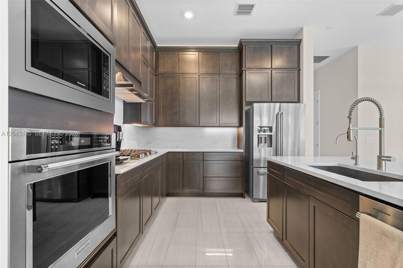 A modern kitchen features dark wood cabinetry, stainless steel appliances, and white stone countertops — 257 Zelda Ln, Delray Beach FL 33445, DELRAY BEACH, FL