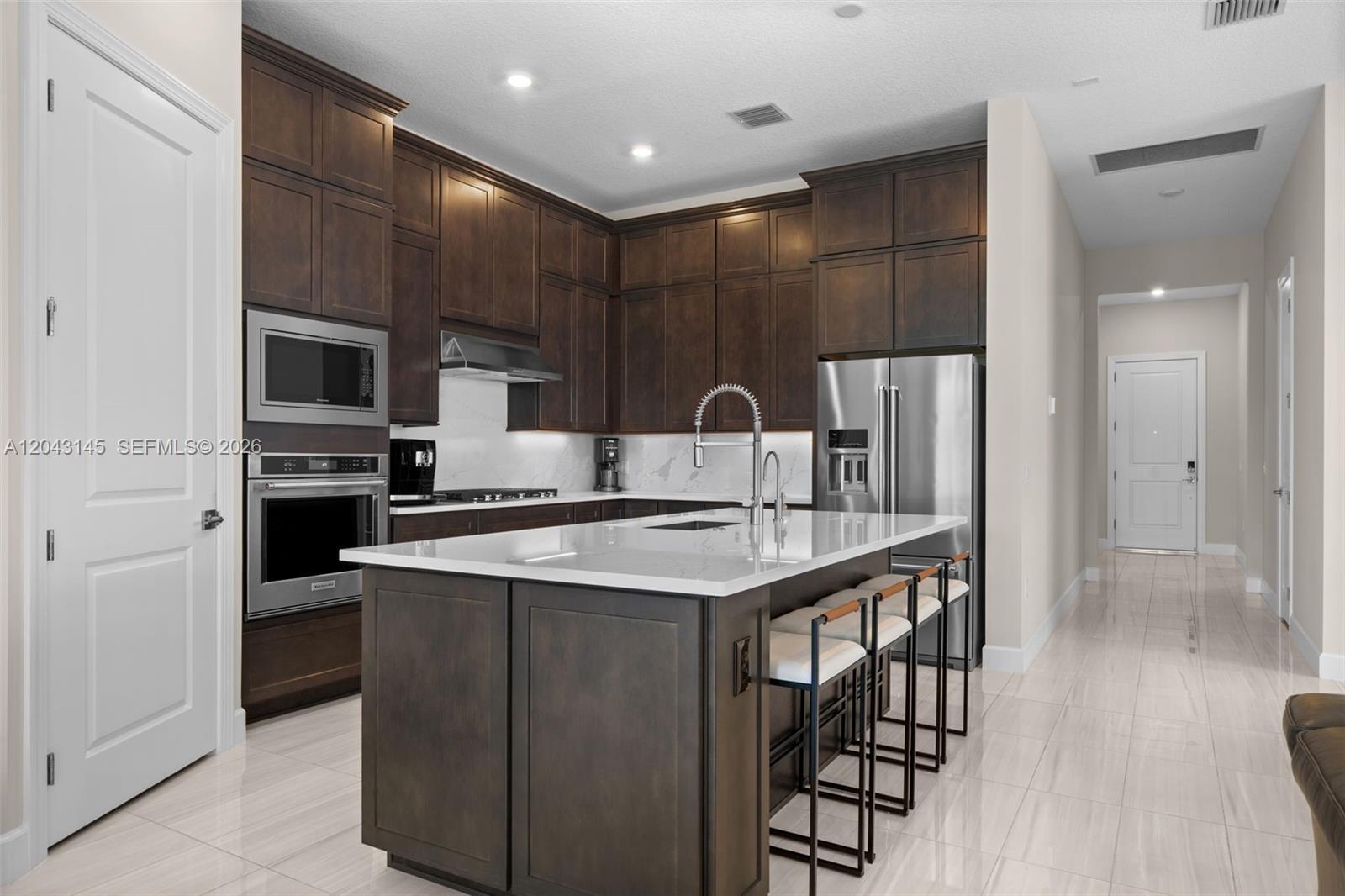 A kitchen features dark wood cabinetry, a white quartz island, and stainless steel appliances — 257 Zelda Ln, Delray Beach FL 33445, DELRAY BEACH, FL