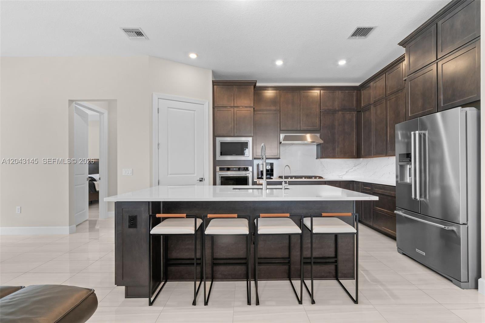 A modern kitchen features dark wood cabinetry, a white quartz island, and stainless steel appliances — 257 Zelda Ln, Delray Beach FL 33445, DELRAY BEACH, FL