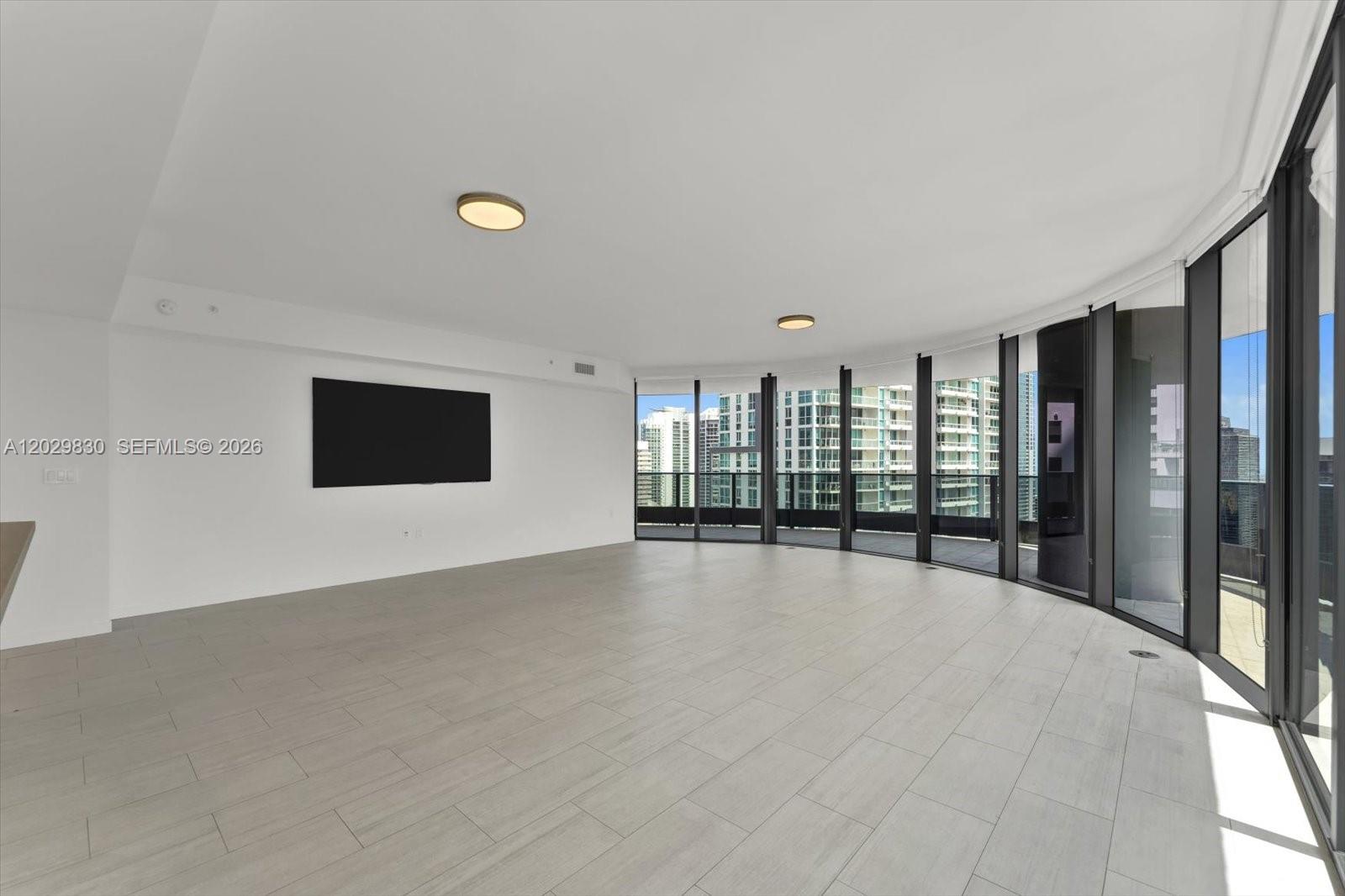 A spacious, empty living room features light-colored tile floors, recessed lighting, and floor-to-ceiling windows — 1000 Brickell Plaza # 3602, Miami FL 33131, MIAMI, FL