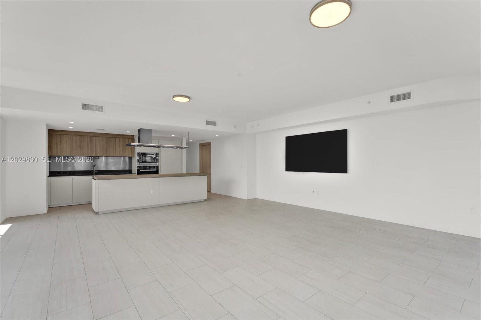 A modern, open-concept living area features a kitchen with wood cabinets and light tile flooring — 1000 Brickell Plaza # 3602, Miami FL 33131, MIAMI, FL