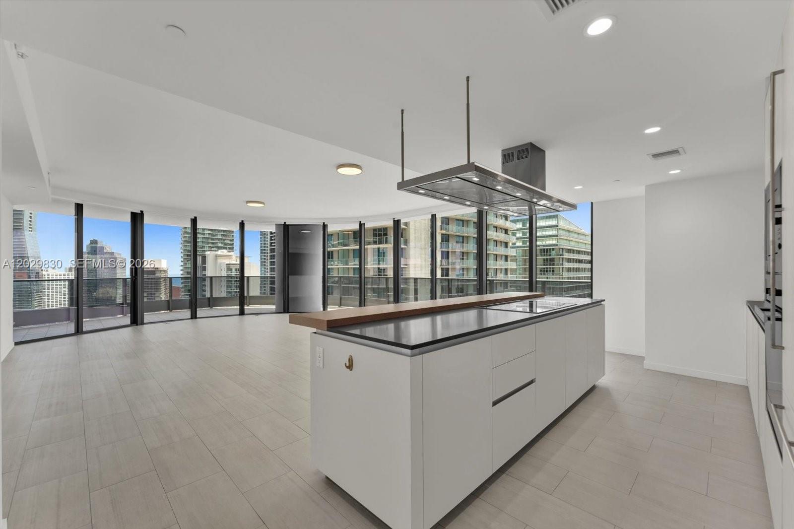 A modern kitchen with a large island and floor-to-ceiling windows overlooking a city skyline — 1000 Brickell Plaza # 3602, Miami FL 33131, MIAMI, FL