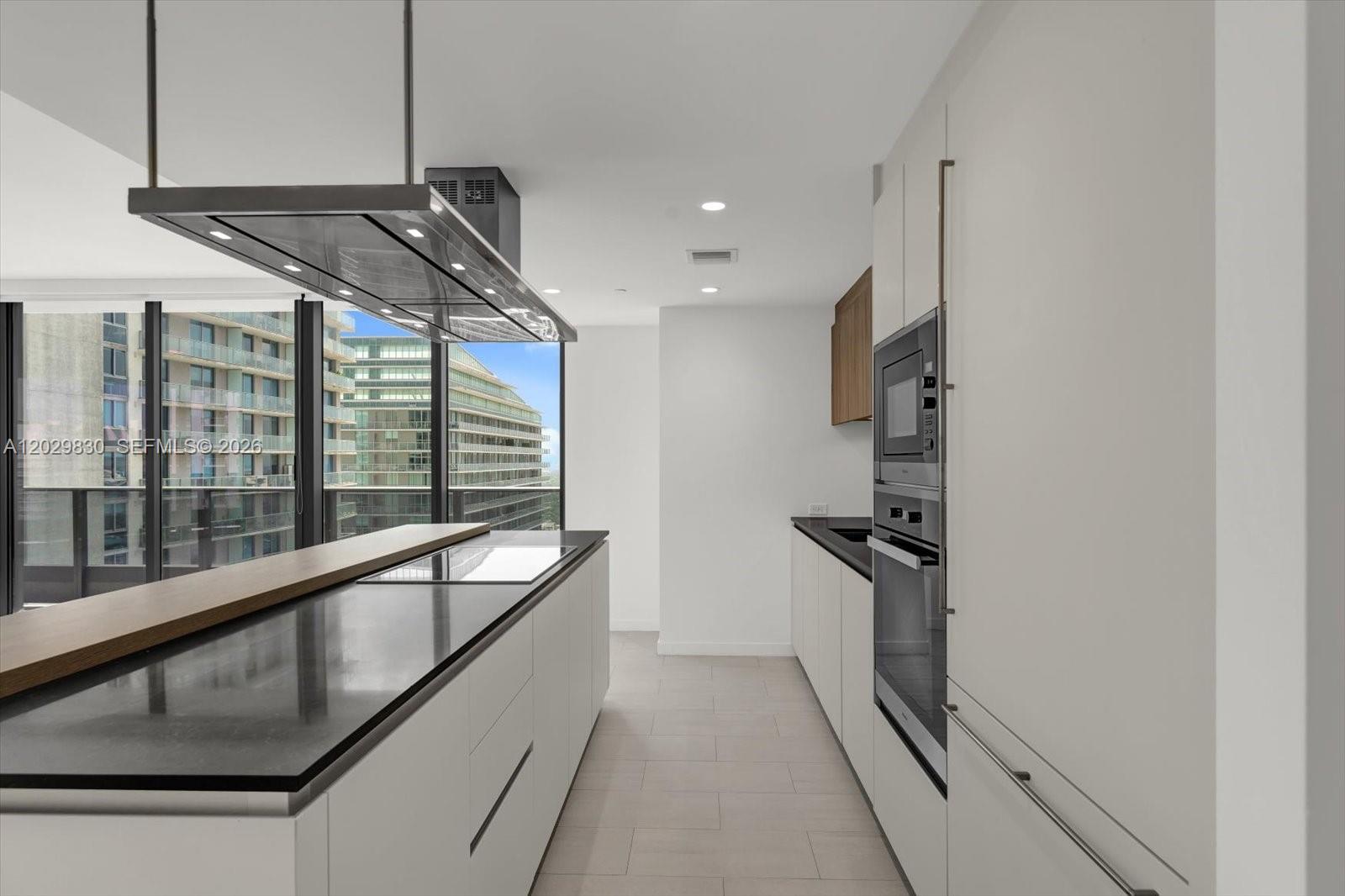 A modern kitchen features a large island with a cooktop, stainless appliances, and floor-to-ceiling windows — 1000 Brickell Plaza # 3602, Miami FL 33131, MIAMI, FL
