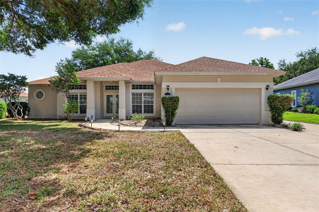 A single-story house with a beige stucco exterior, a two-car garage, and a brown roof — 39914 SUNBEAM WAY, LADY LAKE, FL