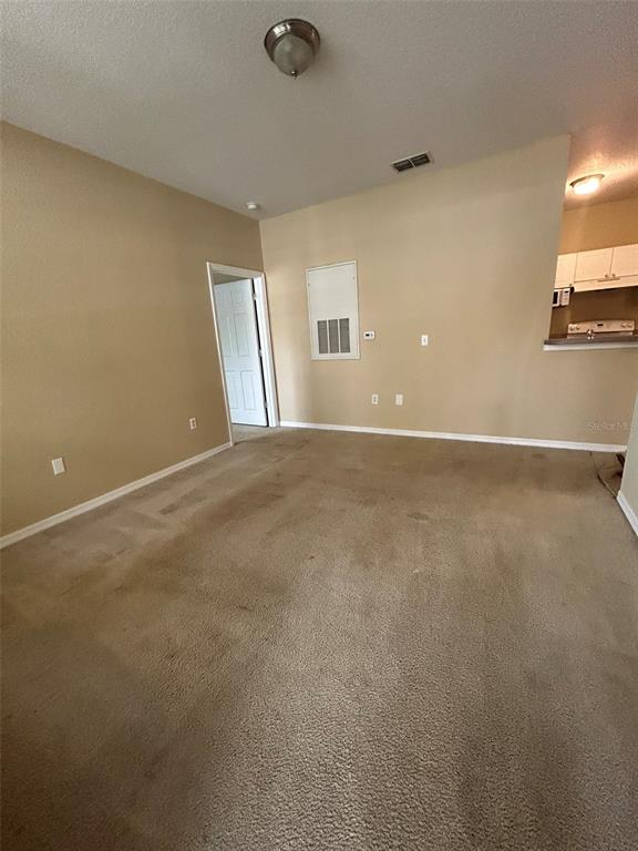 An empty living room with beige carpet, tan walls, and an adjacent kitchen area — 823 GRAND REGENCY POINT UNIT 102, ALTAMONTE SPRINGS, FL