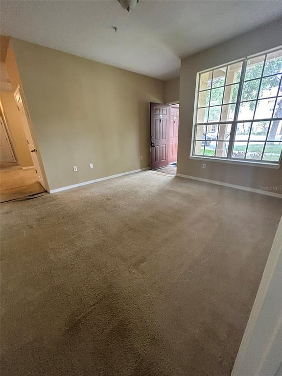 An empty living room features beige carpet, tan walls, and a large window — 823 GRAND REGENCY POINT UNIT 102, ALTAMONTE SPRINGS, FL