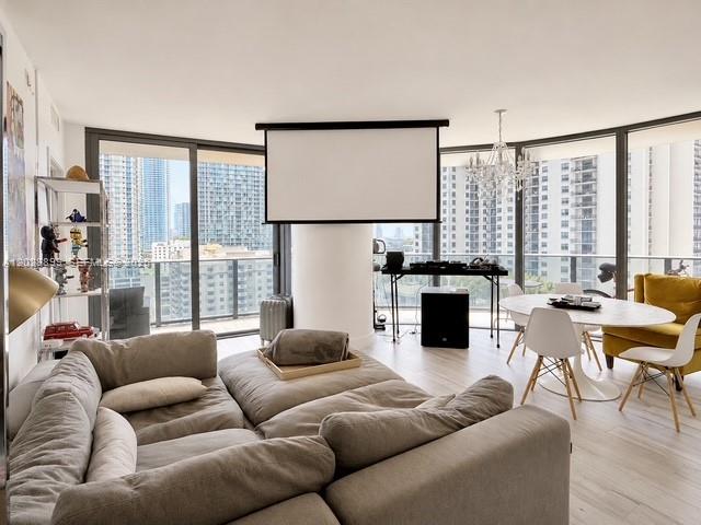 A modern living room features a large sectional sofa, a projector screen, and floor-to-ceiling windows — 45 SW 9th St # 1506, Miami FL 33130, MIAMI, FL