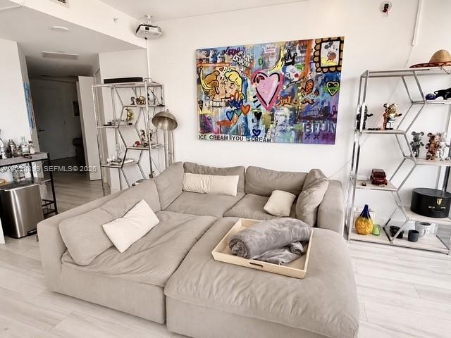 A living room features a large beige sectional sofa, metal shelving units, and colorful wall art — 45 SW 9th St # 1506, Miami FL 33130, MIAMI, FL