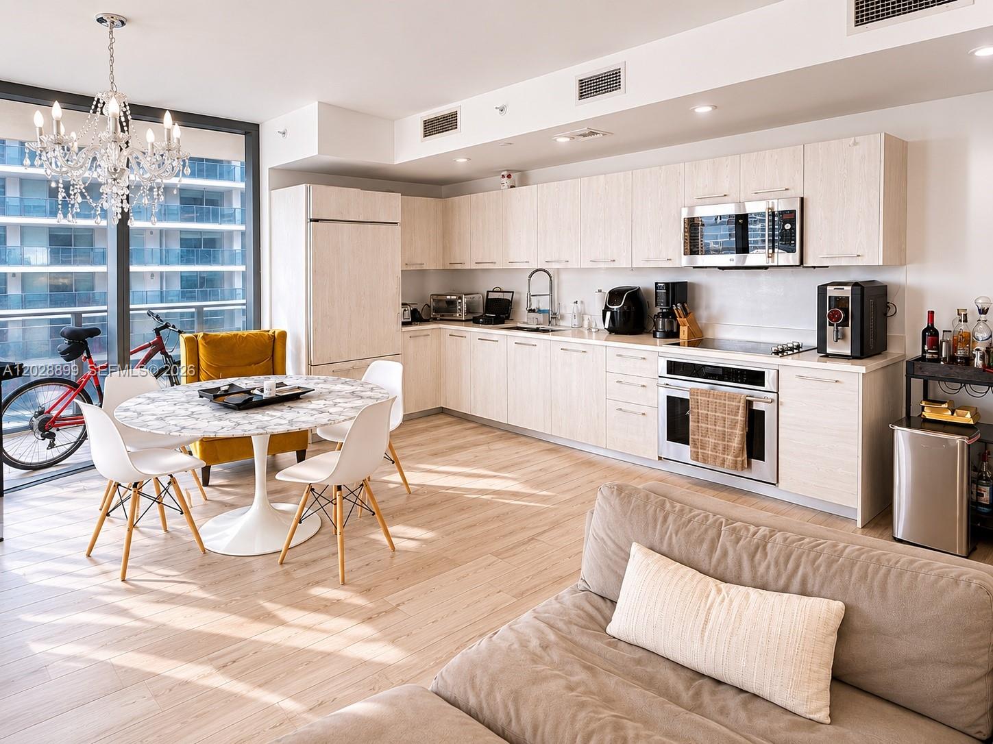 A modern kitchen and dining area features light wood cabinetry, white chairs, and a chandelier — 45 SW 9th St # 1506, Miami FL 33130, MIAMI, FL