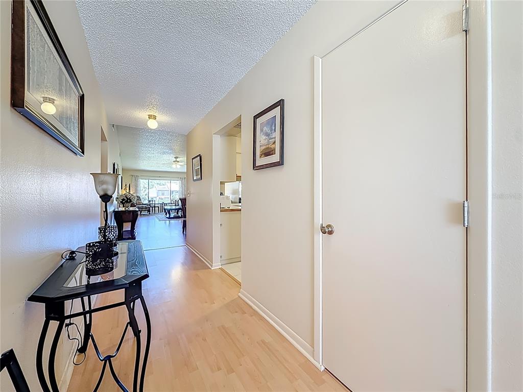 A hallway with light wood flooring leads to an open living area with a kitchen — 3505 TARPON WOODS BLVD UNIT P408, PALM HARBOR, FL