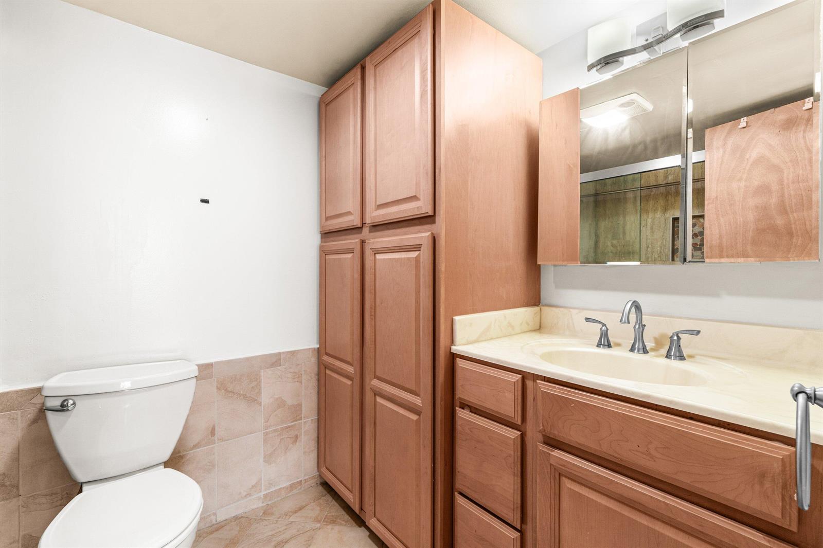 A bathroom features a wooden vanity, a tall storage cabinet, a toilet, and a mirror — 1020 Silk Oak Terrace # 102, Delray Beach FL 33445, DELRAY BEACH, FL