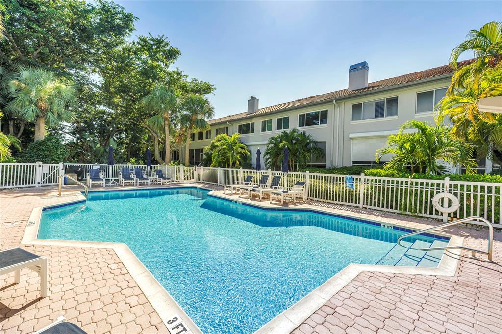 A swimming pool with a brick deck sits in front of a multi-story residential building — 903 PINELLAS BAYWAY S UNIT 302, TIERRA VERDE, FL