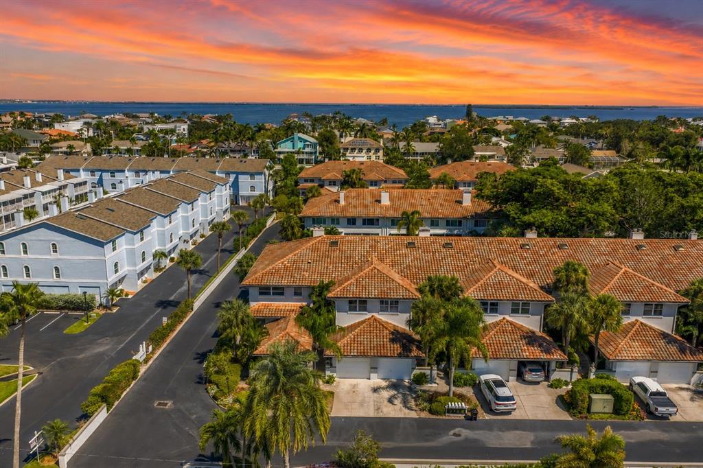An aerial view shows multi-story townhomes with tiled roofs near a body of water at sunset — 903 PINELLAS BAYWAY S UNIT 302, TIERRA VERDE, FL