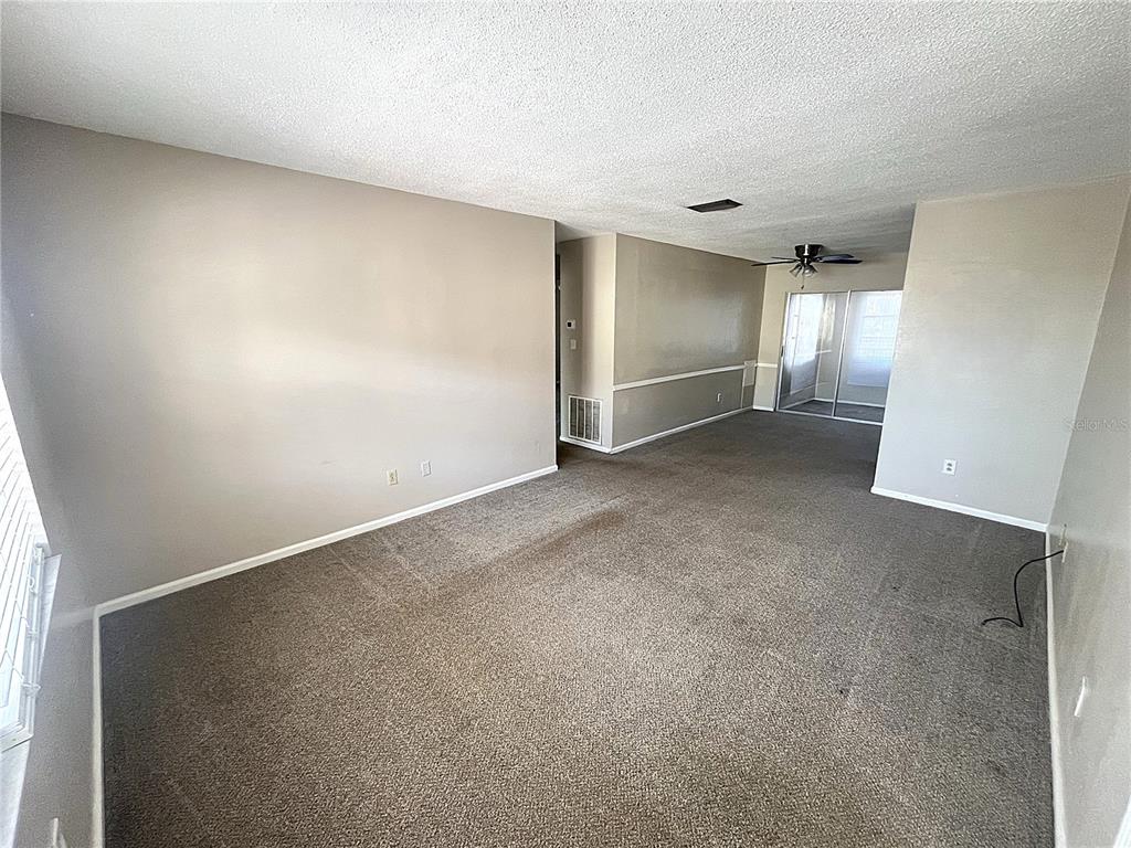 An empty living room features beige walls, brown carpeting, and a sliding glass door — 4507 9TH STREET W UNIT J6, BRADENTON, FL