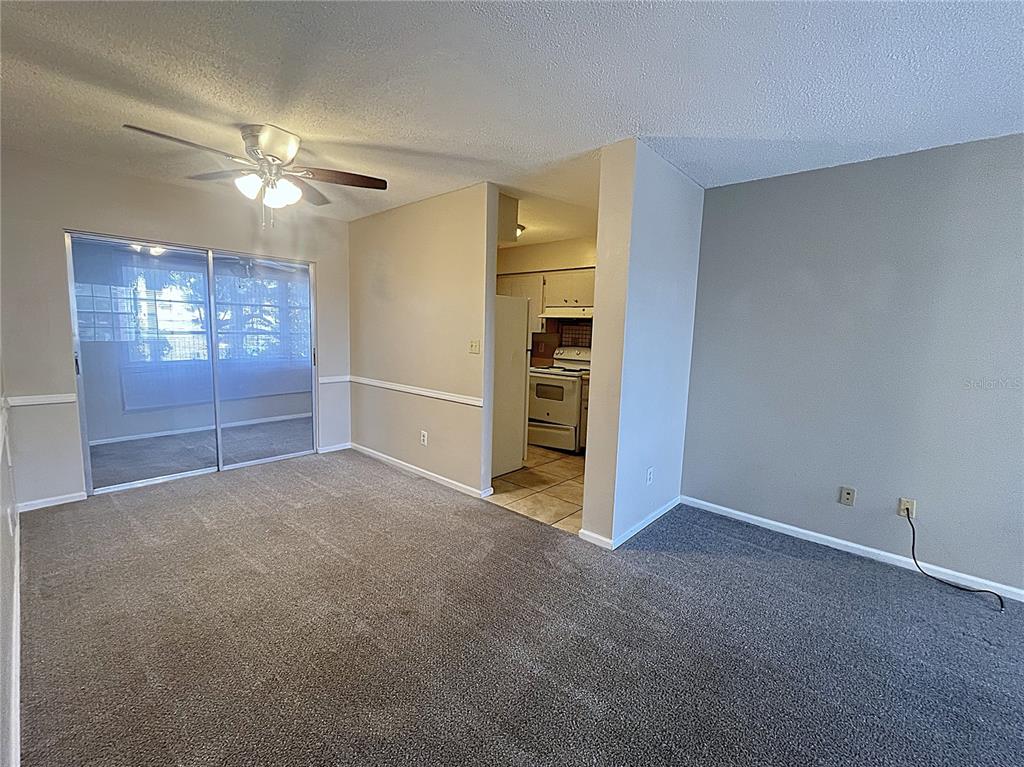 A carpeted living room with a ceiling fan, sliding glass doors, and an adjacent kitchen — 4507 9TH STREET W UNIT J6, BRADENTON, FL