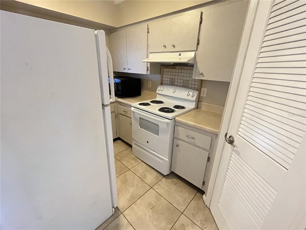 A kitchen features white appliances, light-colored cabinets, a tiled backsplash, and beige floor tiles — 4507 9TH STREET W UNIT J6, BRADENTON, FL