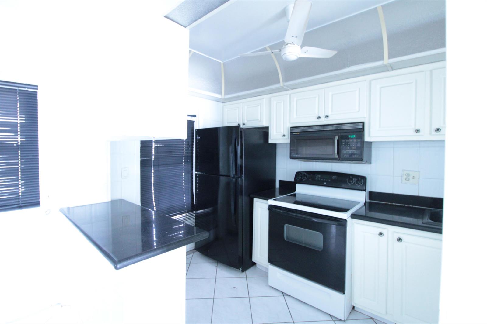 A kitchen features white cabinets, black appliances, black countertops, and white tile flooring — 465 Paradise Isle Boulevard # 110, Hallandale Beach FL 33009, HALLANDALE BEACH, FL