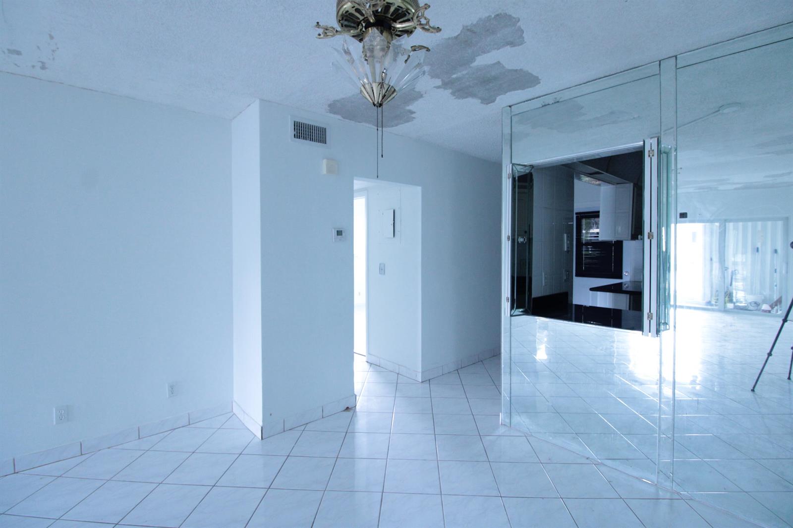 A room with white tile floors, a mirrored wall, and water damage on the ceiling — 465 Paradise Isle Boulevard # 110, Hallandale Beach FL 33009, HALLANDALE BEACH, FL