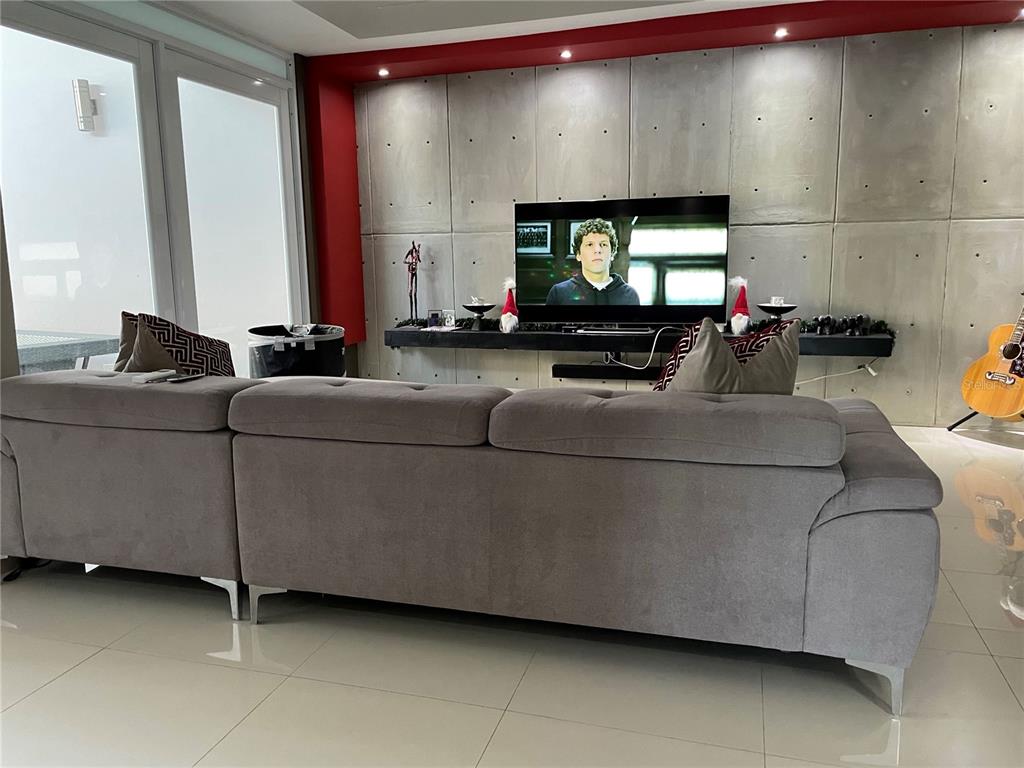 A living room features a grey sectional sofa facing a television mounted on a concrete wall — 7 ALTURAS DE TORRIMAR UNIT 11-7, GUAYNABO, PR