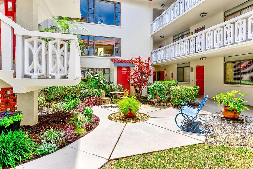 A courtyard with a concrete walkway, landscaping, and a blue metal rocking chair — 2612 PEARCE DRIVE UNIT 209, CLEARWATER, FL