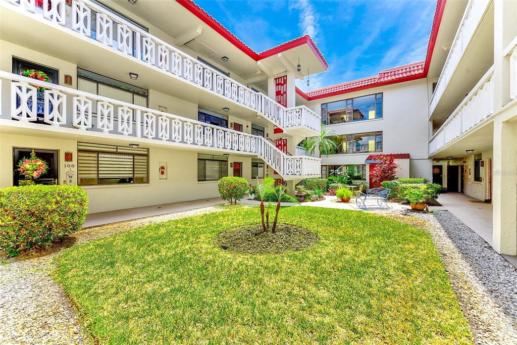 An exterior view of a multi-story apartment complex with a central grassy courtyard — 2612 PEARCE DRIVE UNIT 209, CLEARWATER, FL