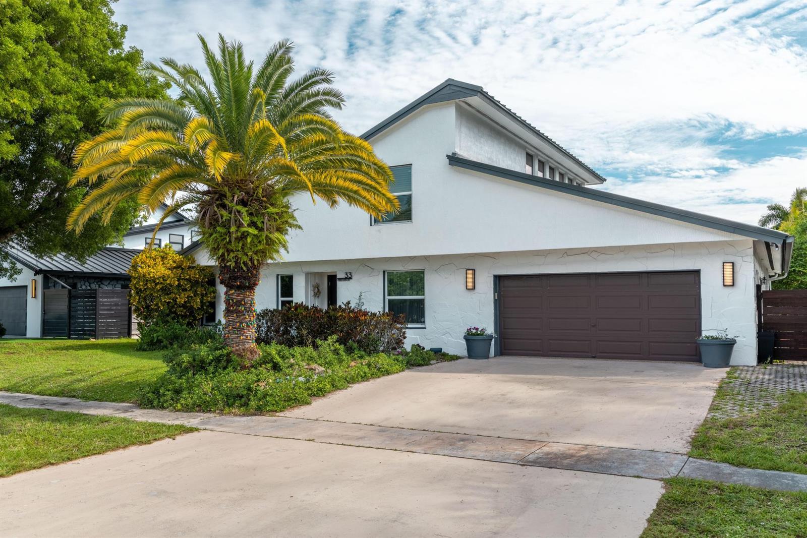 A white two-story house features a brown garage door, a palm tree, and a driveway — 33 Oregon Lane, Boca Raton FL 33487, BOCA RATON, FL
