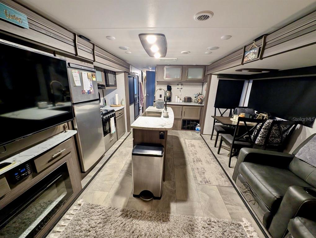 A modern RV interior featuring a kitchen island, stainless steel appliances, and a dining area — 25338 NE 141ST STREET, SALT SPRINGS, FL