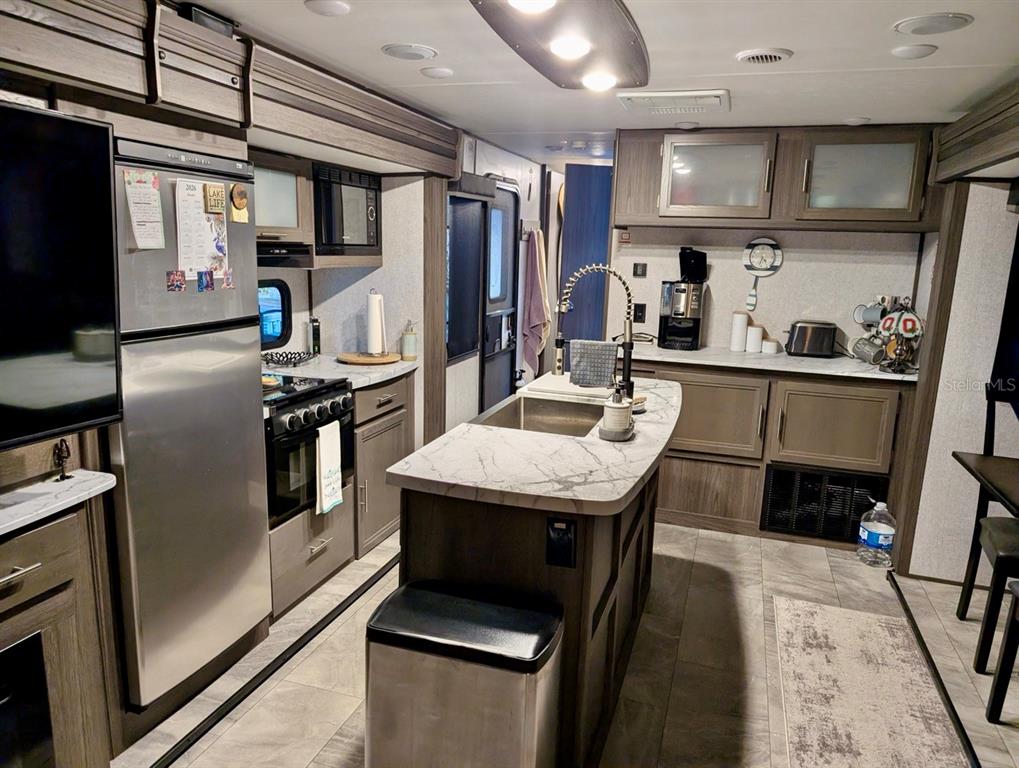 A modern RV kitchen features a center island, stainless steel appliances, and wood-toned cabinetry — 25338 NE 141ST STREET, SALT SPRINGS, FL