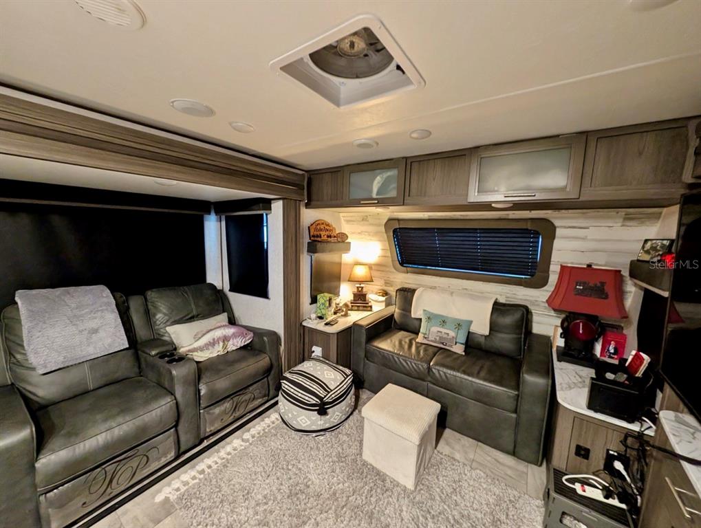 A living area in an RV features gray leather furniture, a rug, and overhead cabinets — 25338 NE 141ST STREET, SALT SPRINGS, FL