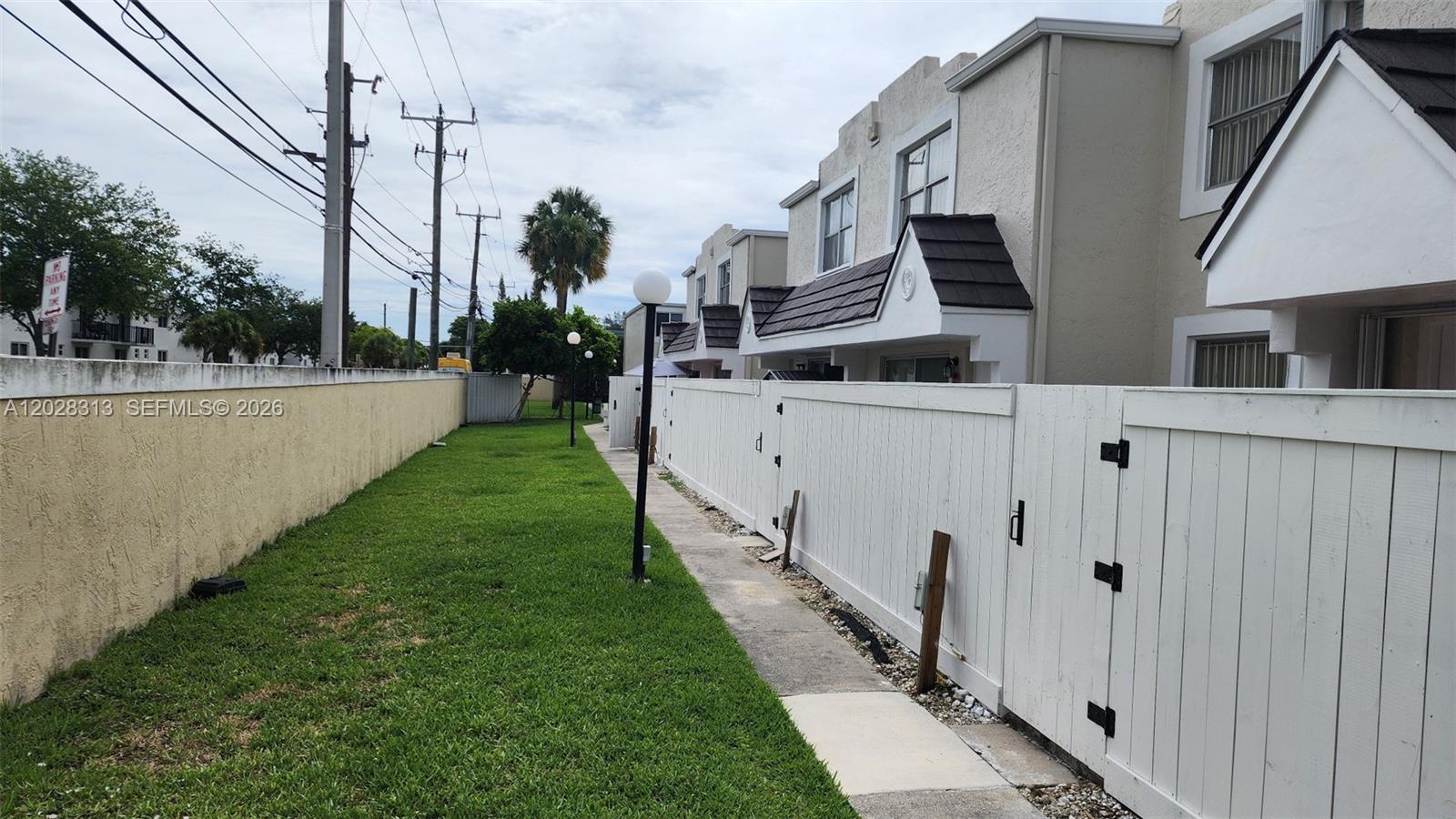A grassy side yard runs between a beige wall and a white wooden fence — 4540 SW 68th Ct Cir # 7, Miami FL 33155, MIAMI, FL