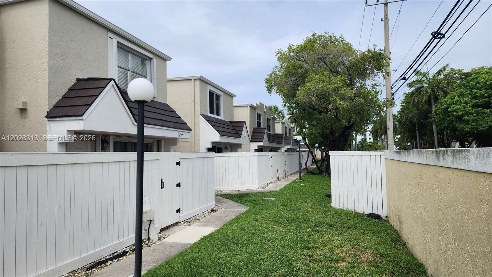 A row of townhouses features white privacy fences, dark shingled roofs, and a grassy walkway — 4540 SW 68th Ct Cir # 7, Miami FL 33155, MIAMI, FL