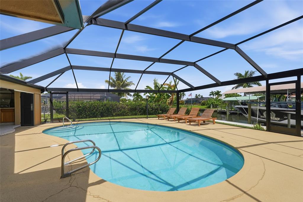 A screened-in pool area features a kidney-shaped pool, lounge chairs, and a canal view — 418 AVALON DRIVE, CAPE CORAL, FL