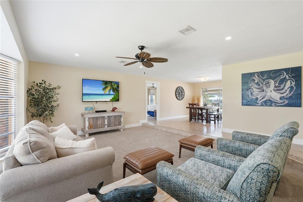 A living room features beige carpet, a ceiling fan, a television, and blue patterned armchairs — 418 AVALON DRIVE, CAPE CORAL, FL