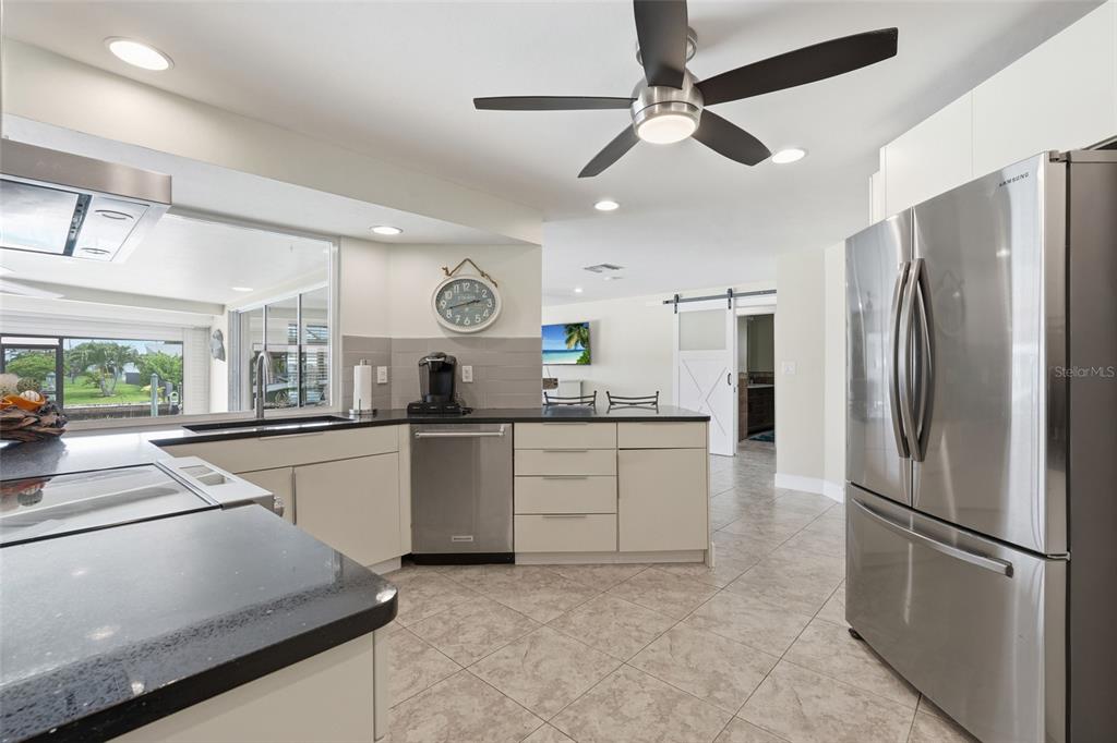 A modern kitchen features light-colored cabinetry, black countertops, stainless steel appliances, and a ceiling fan — 418 AVALON DRIVE, CAPE CORAL, FL