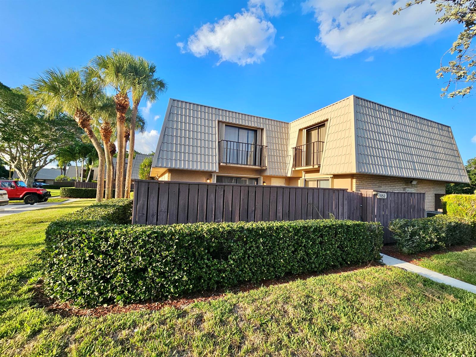 A two-story townhouse with a mansard roof, a wooden privacy fence, and palm trees — 5152 51st Way, West Palm Beach FL 33409, WEST PALM BEACH, FL