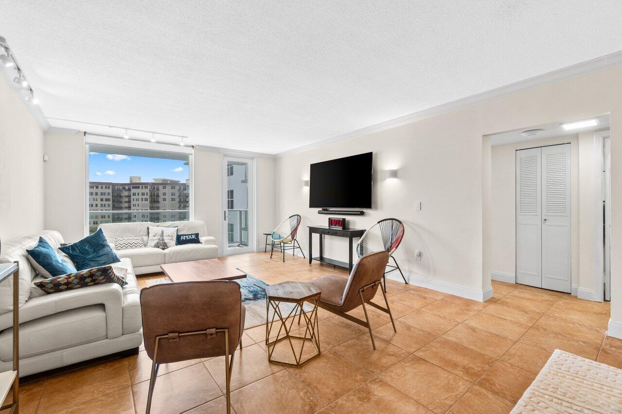 A living room features tile flooring, a white sofa, a wall-mounted television, and balcony access — 3450 S Ocean Boulevard # 5150, Palm Beach FL 33480, PALM BEACH, FL
