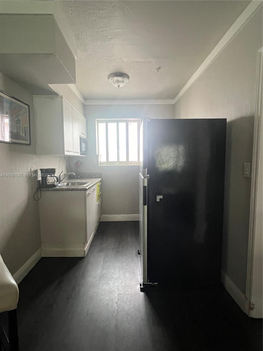 A galley-style kitchen features white cabinets, a black refrigerator, and dark flooring — 1524 Lenox Ave # 11, Miami Beach FL 33139, MIAMI BEACH, FL
