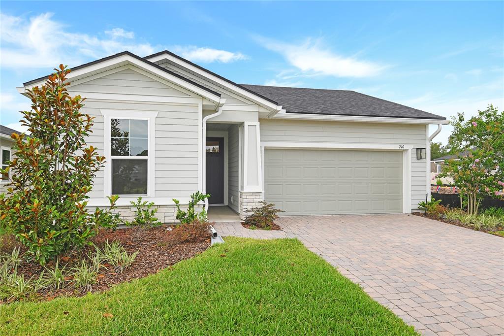 A single-story house with light gray siding, a stone base, and a paved driveway — 210 ENCLAVE AVENUE, PALM COAST, FL