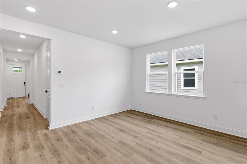 An empty room with light wood-look flooring, white walls, recessed lighting, and two windows — 210 ENCLAVE AVENUE, PALM COAST, FL