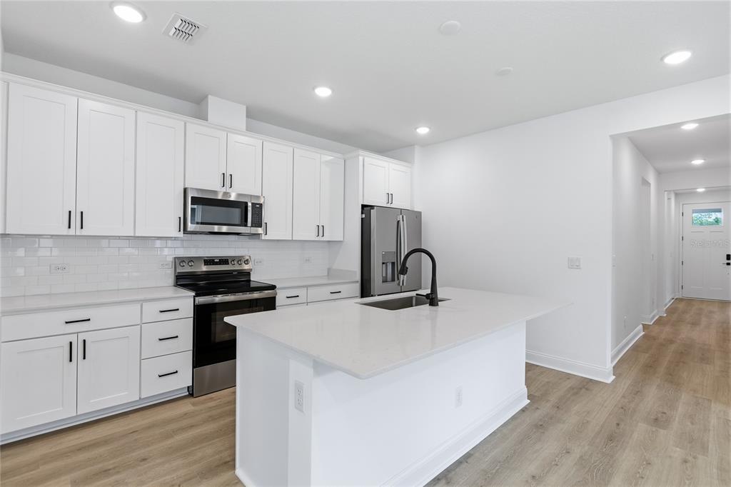 A modern kitchen features white cabinetry, stainless steel appliances, and a central island with seating — 210 ENCLAVE AVENUE, PALM COAST, FL