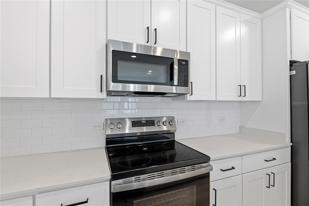 A kitchen features white cabinets, a stainless steel microwave, a black stove, and subway tile — 210 ENCLAVE AVENUE, PALM COAST, FL