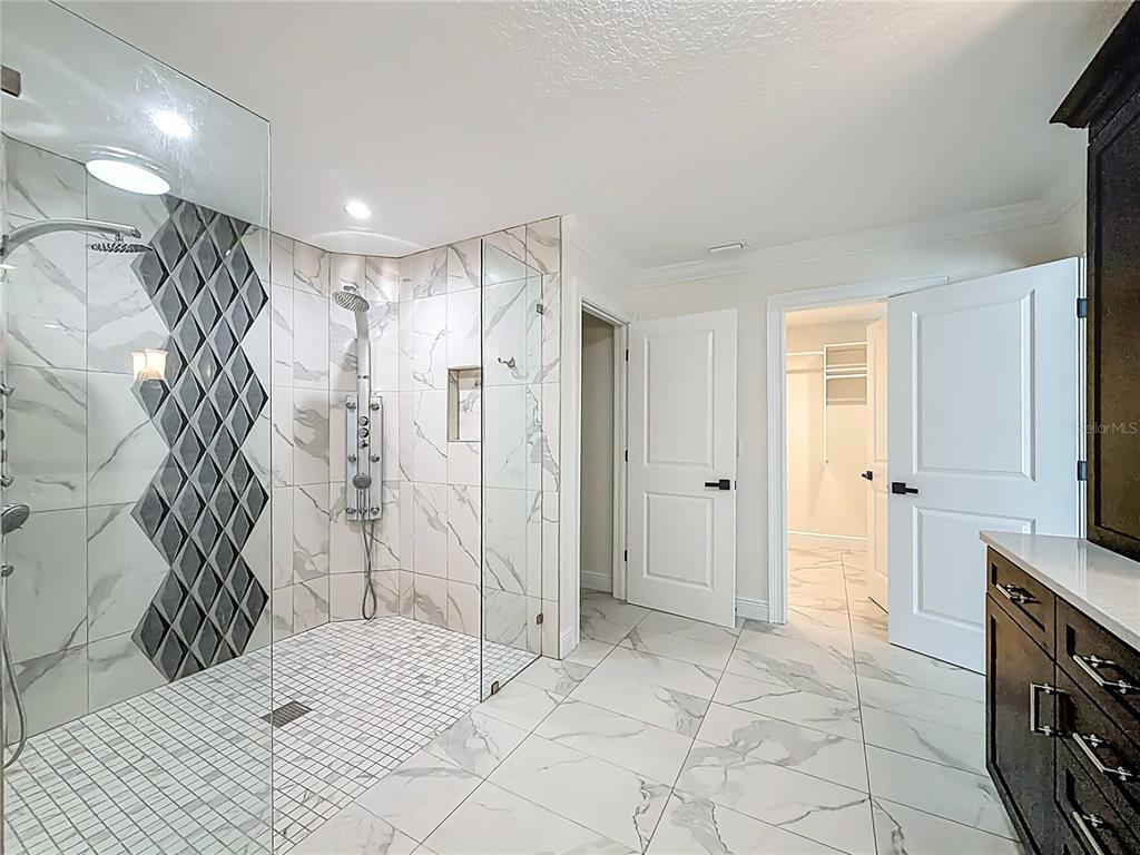 A modern bathroom features a glass-enclosed walk-in shower with marble-look tile and dark accents — 3575 SW 24TH AVENUE ROAD, OCALA, FL