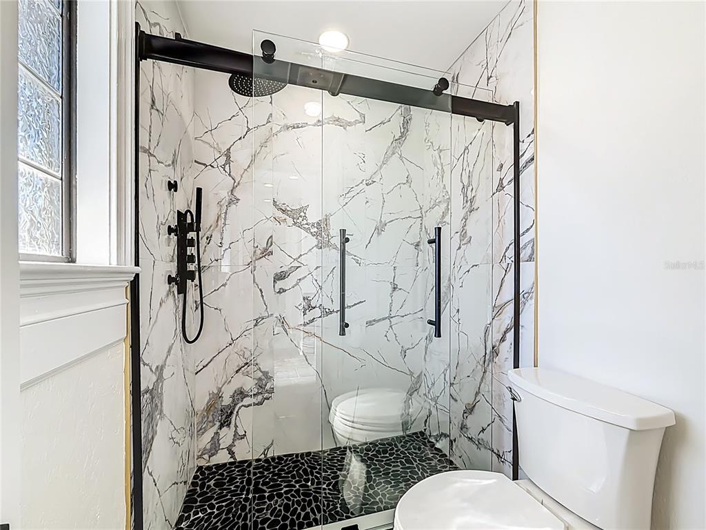 A bathroom features a walk-in shower with marble-patterned tile, black fixtures, and pebble flooring — 3575 SW 24TH AVENUE ROAD, OCALA, FL