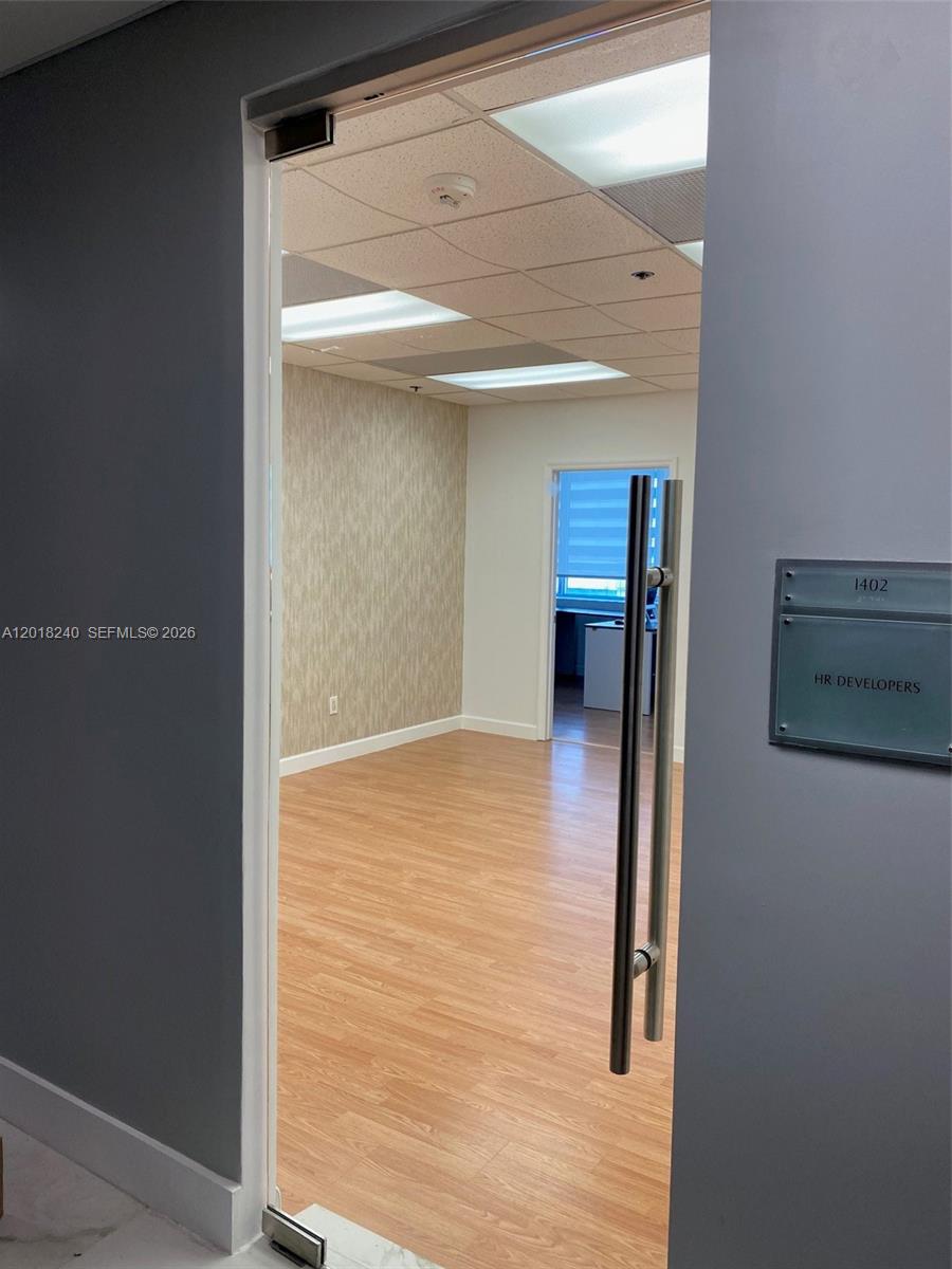An open office suite features light wood-look flooring, a textured accent wall, and glass doors — 150 SE 2nd Ave # 1402, Miami FL 33131, MIAMI, FL