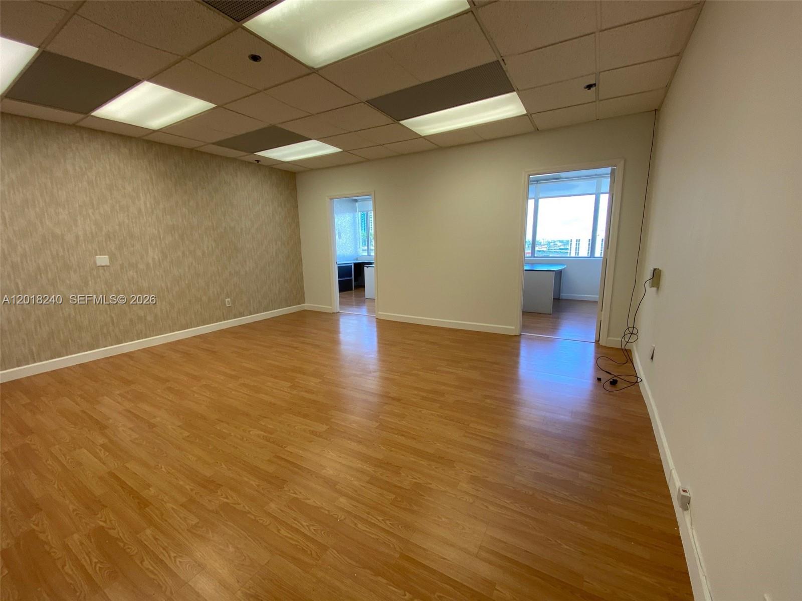 An empty office space features wood-look flooring, a textured accent wall, and two doorways — 150 SE 2nd Ave # 1402, Miami FL 33131, MIAMI, FL