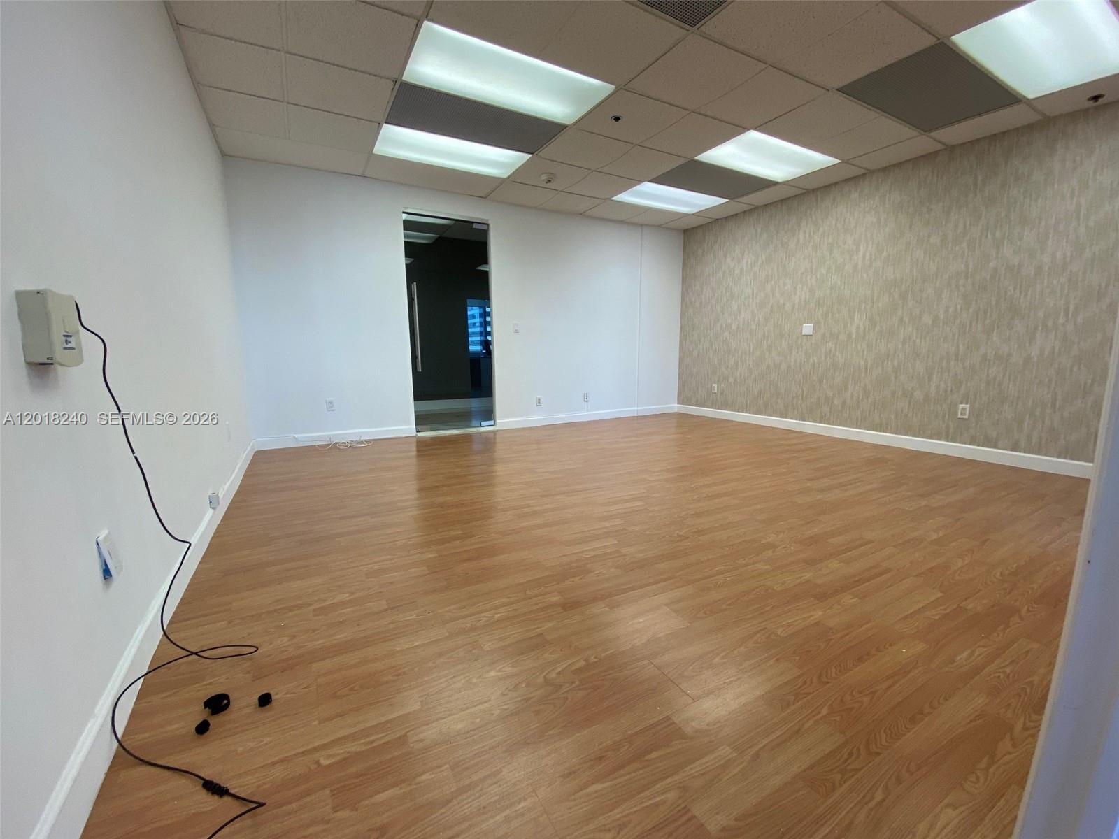 An empty office room features wood-look flooring, white walls, a textured accent wall, and ceiling lights — 150 SE 2nd Ave # 1402, Miami FL 33131, MIAMI, FL