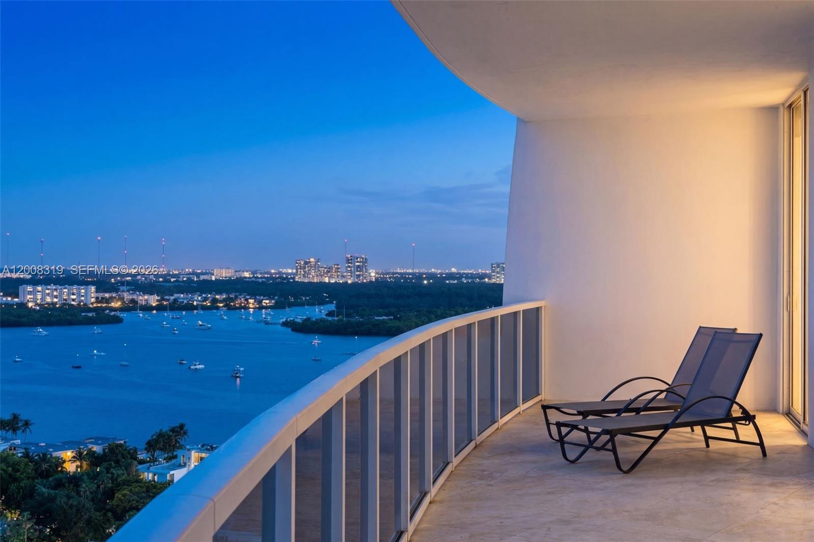 A balcony with two lounge chairs overlooks a bay and city skyline at dusk — 10225 Collins Ave # 2004, Bal Harbour FL 33154, BAL HARBOUR, FL