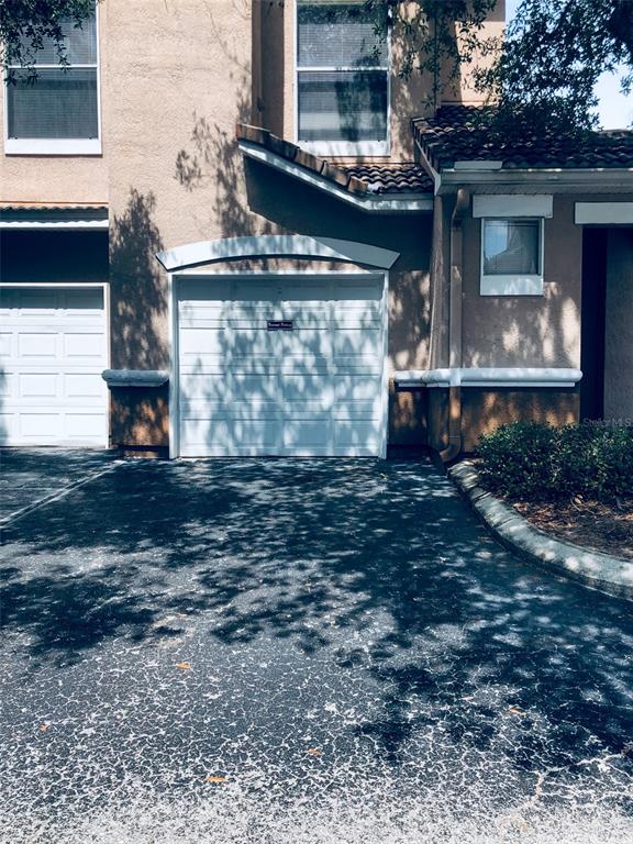 A two-story tan stucco building features a white garage door and a small window — 10561 VILLA VIEW CIRCLE UNIT 10561, TAMPA, FL